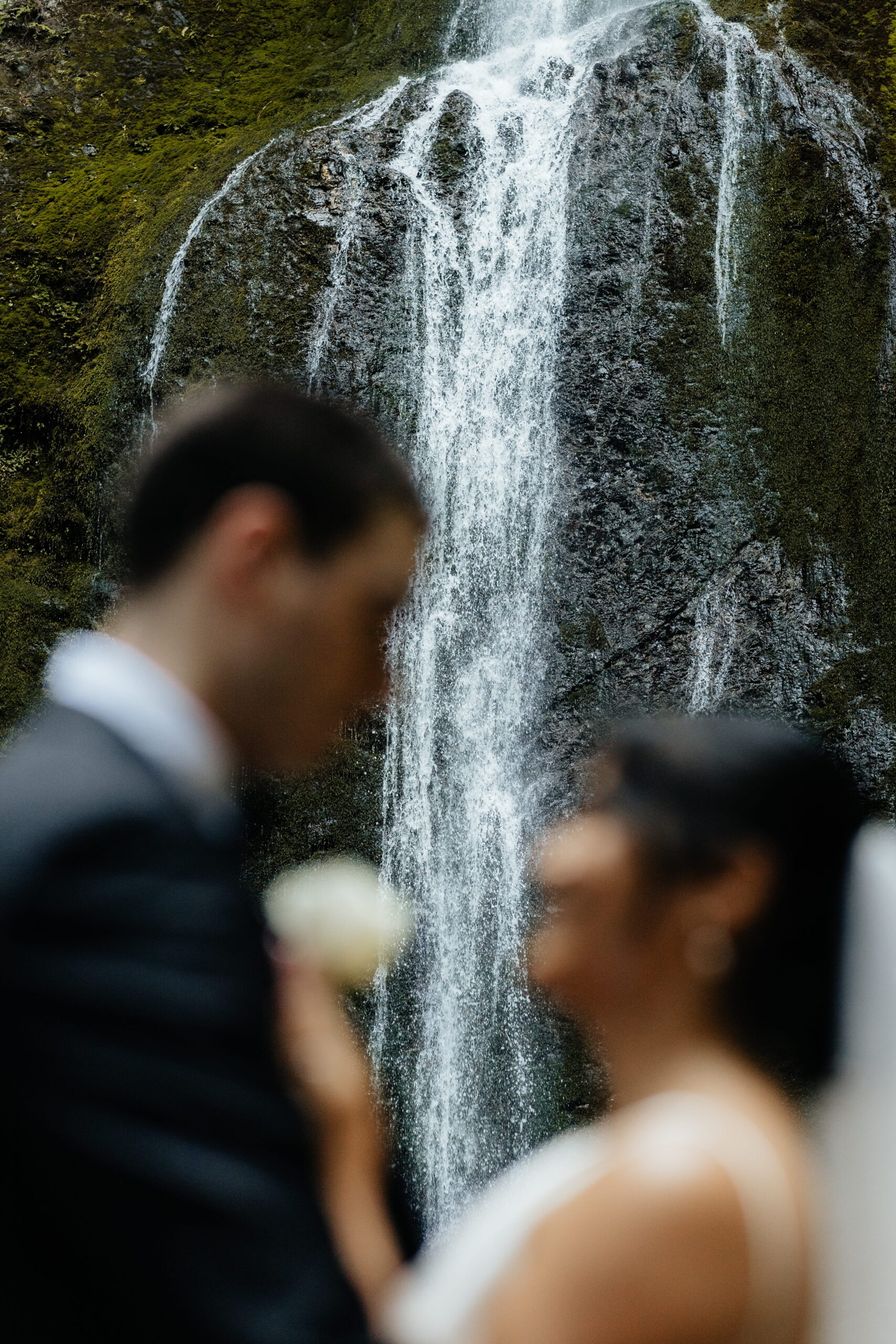 Bride and groom stand in front of Marymere Falls during their elopement in Olympic National Park.