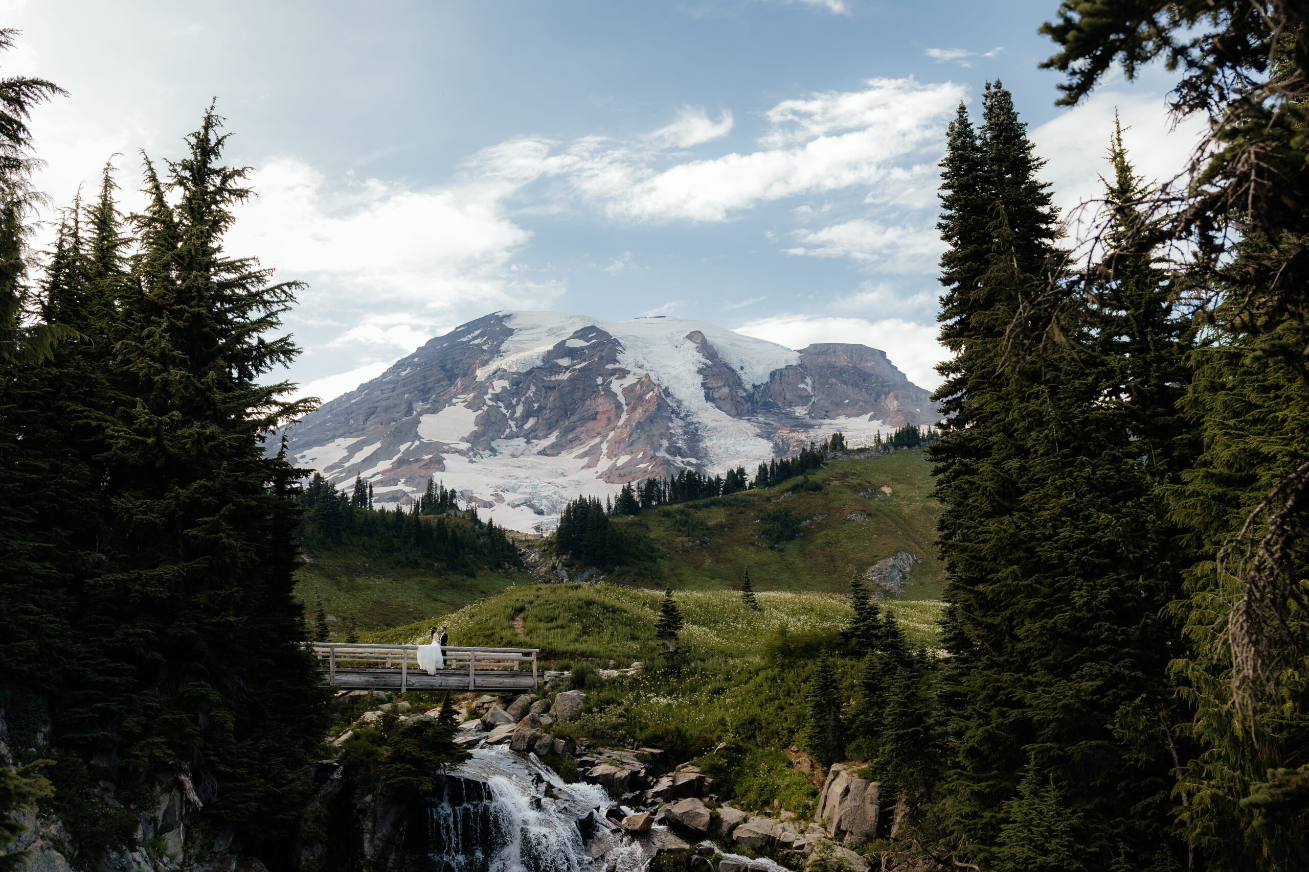 Couple stands on a wood bridge above a waterfall during their Mt Rainier elopement.