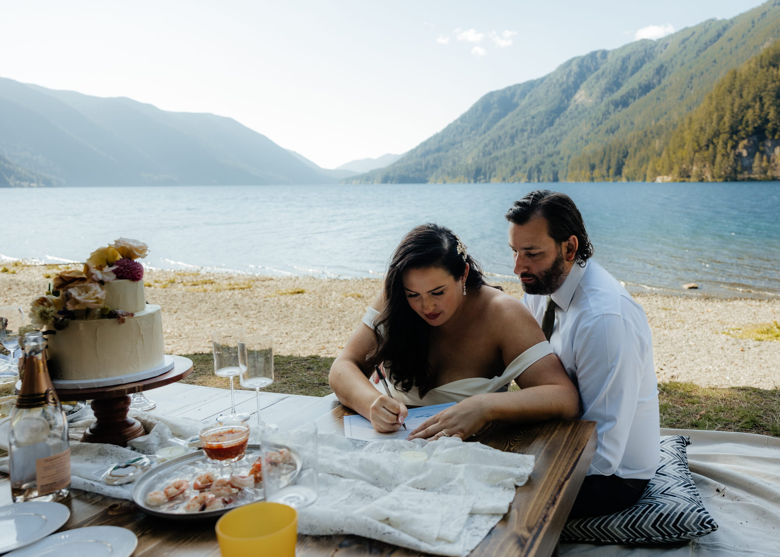 Newlyweds sign their marriage license during an outdoor beach picnic at Lake Crescent.