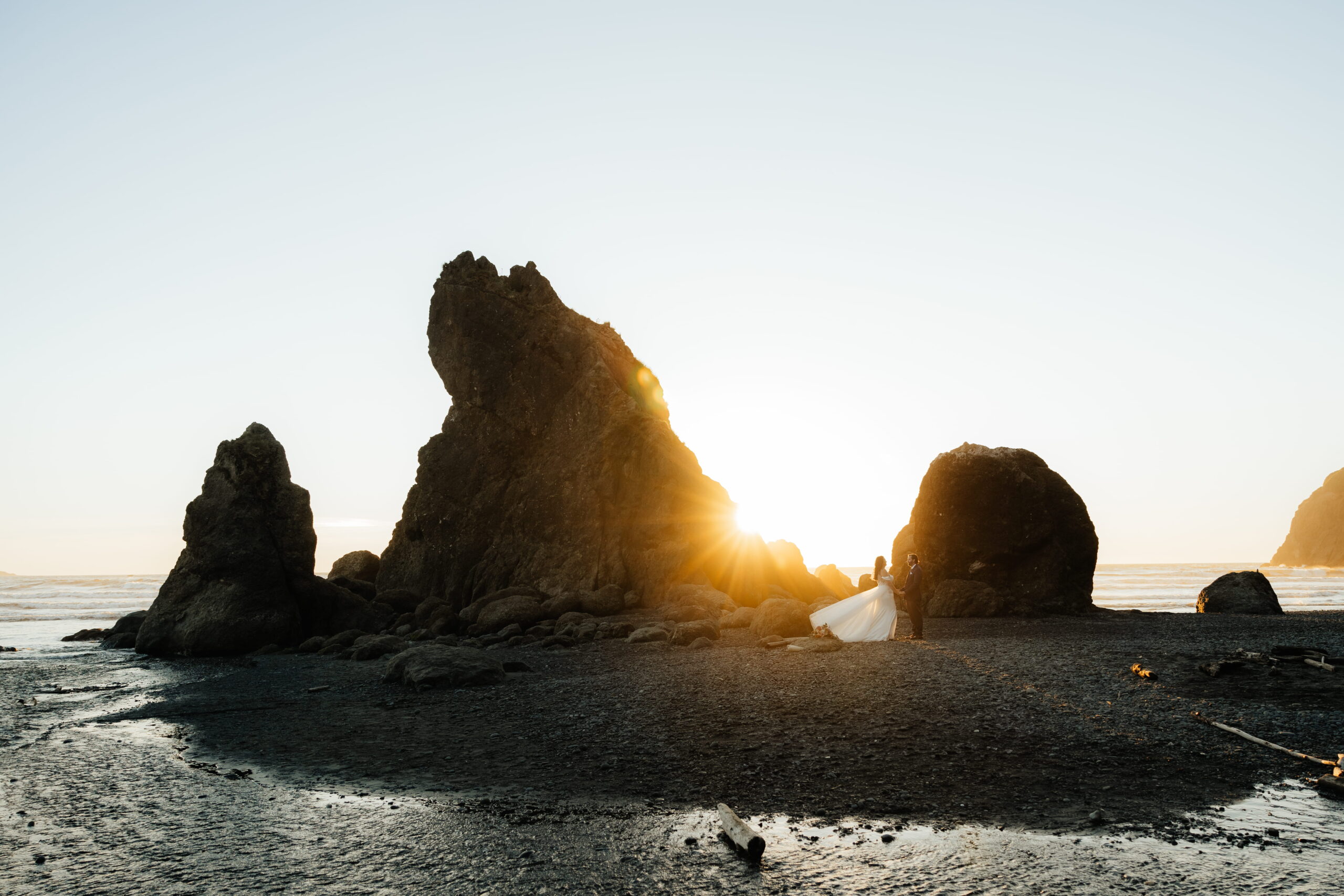 Newlyweds stand next to a sea stack rock at sunset during their Ruby Beach elopement.