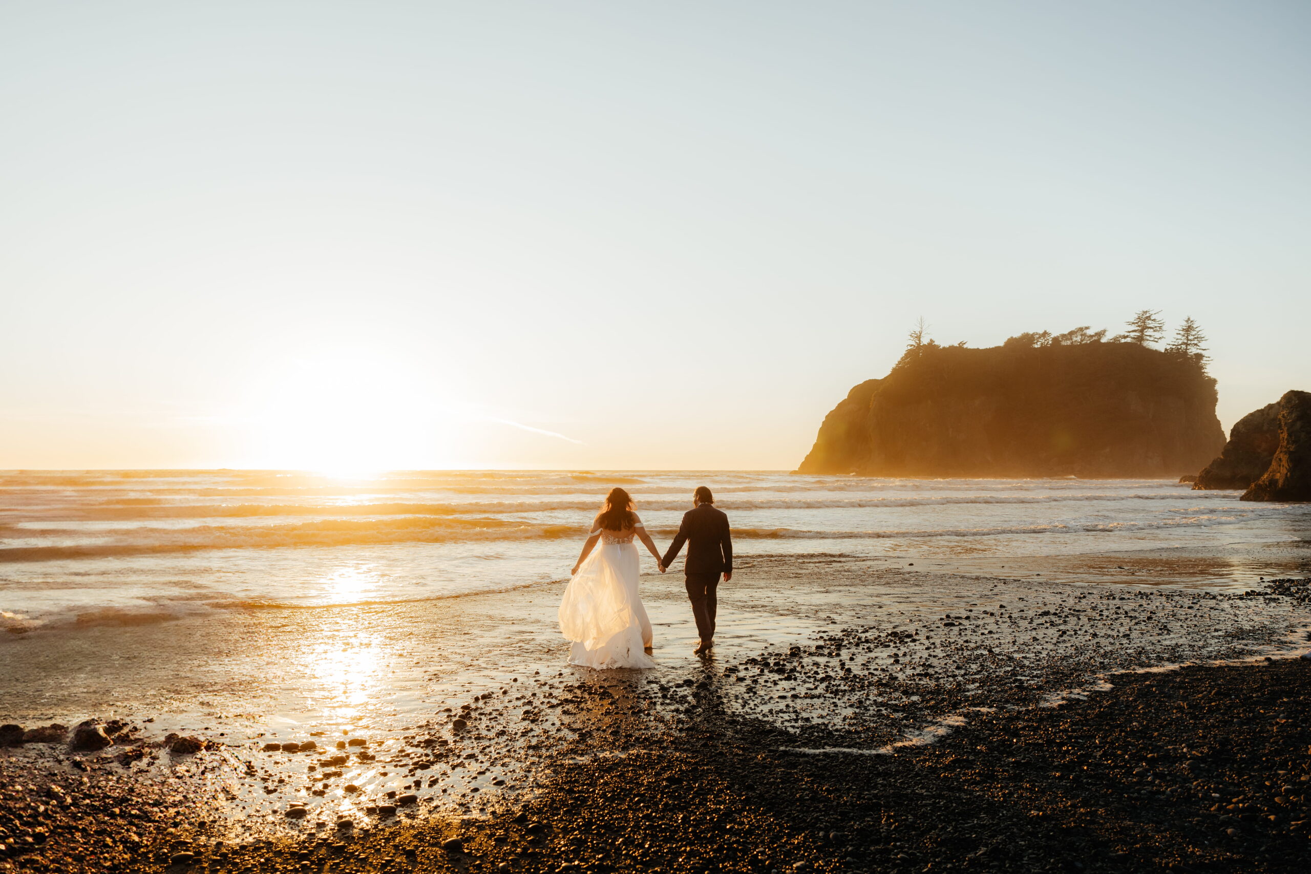 Newlyweds hold hands while walking towards the water during their elopement at Ruby Beach, Washington. 