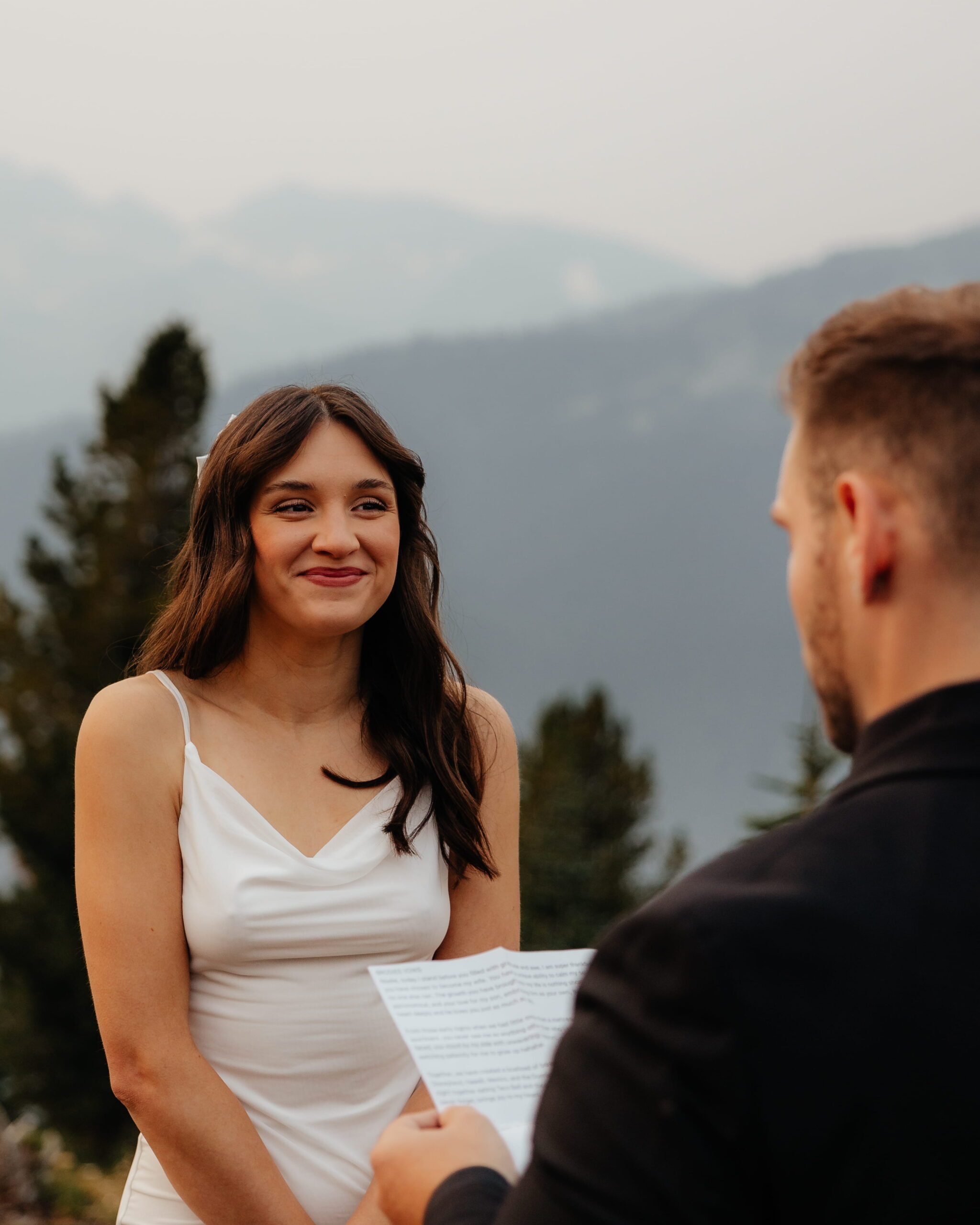 Bride smiles while groom reads vows during their Mt Rainier National Park wedding ceremony.