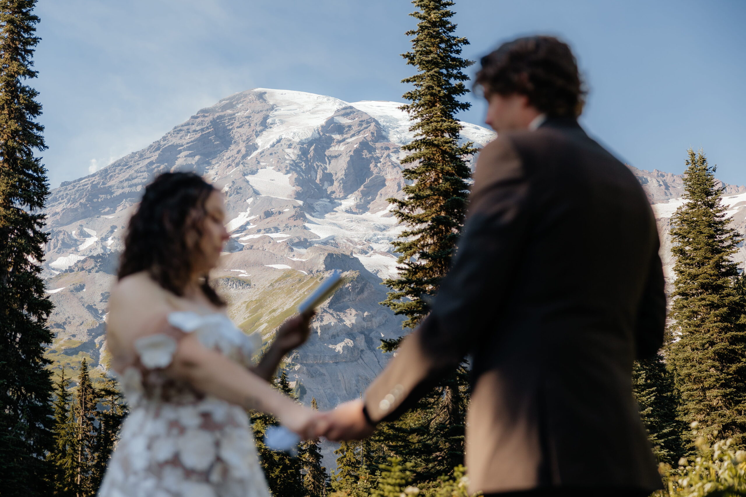 Newlyweds hold hands while reading vows at their Mt Rainier elopement ceremony.