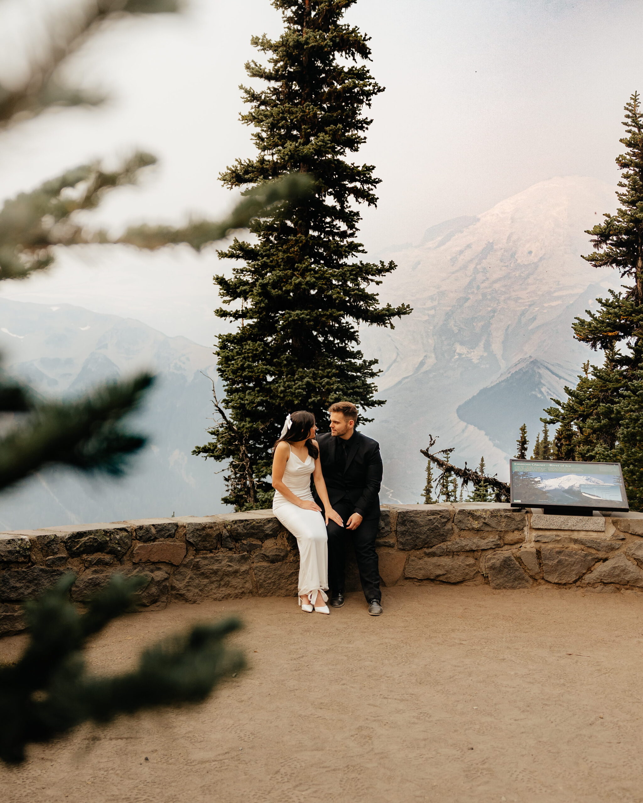 Bride and groom sit on a stone wall during their Sunrise Mt Rainier elopement.