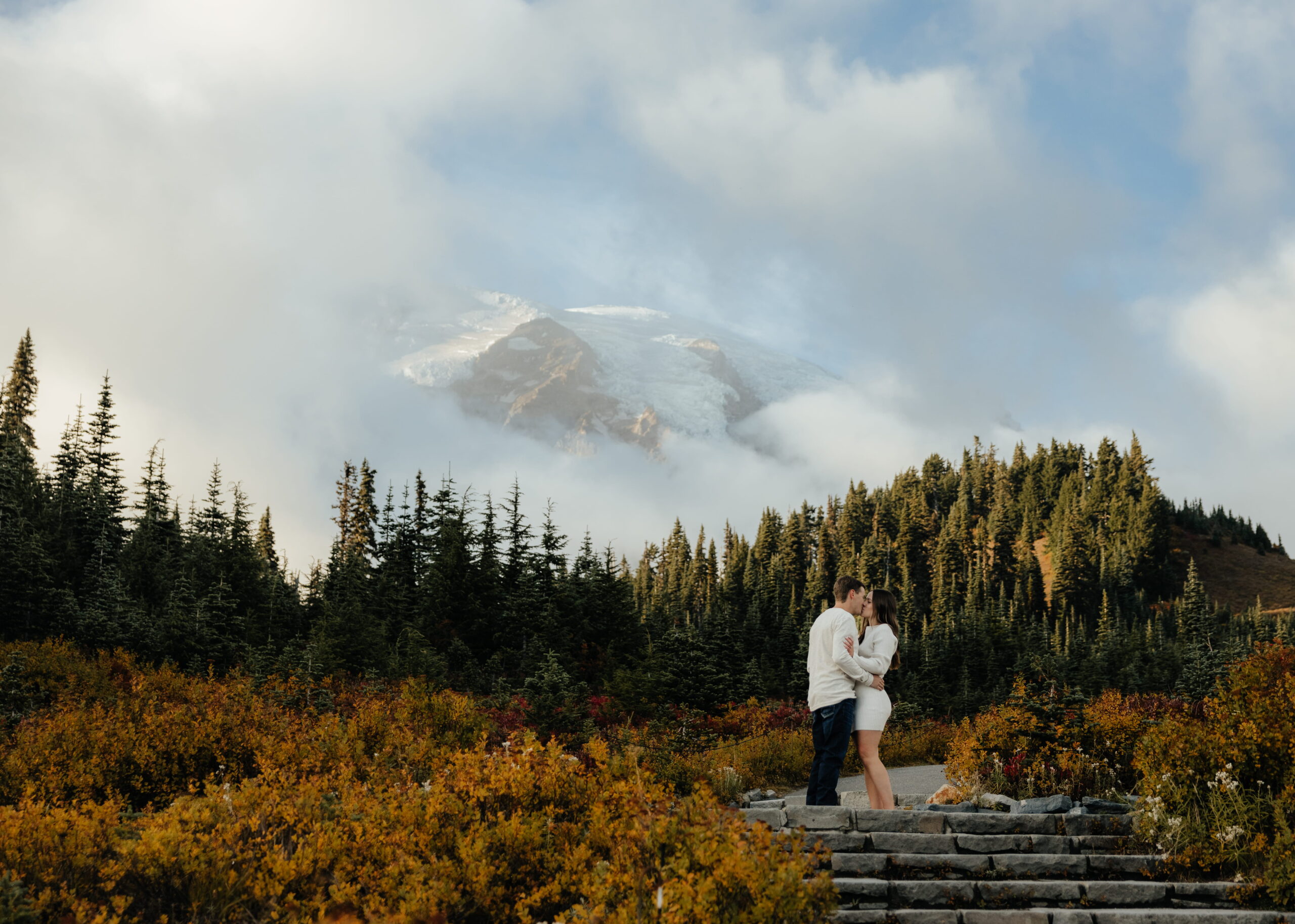 Couple kisses on steps in front of Mt. Rainier during their autumn photo session.