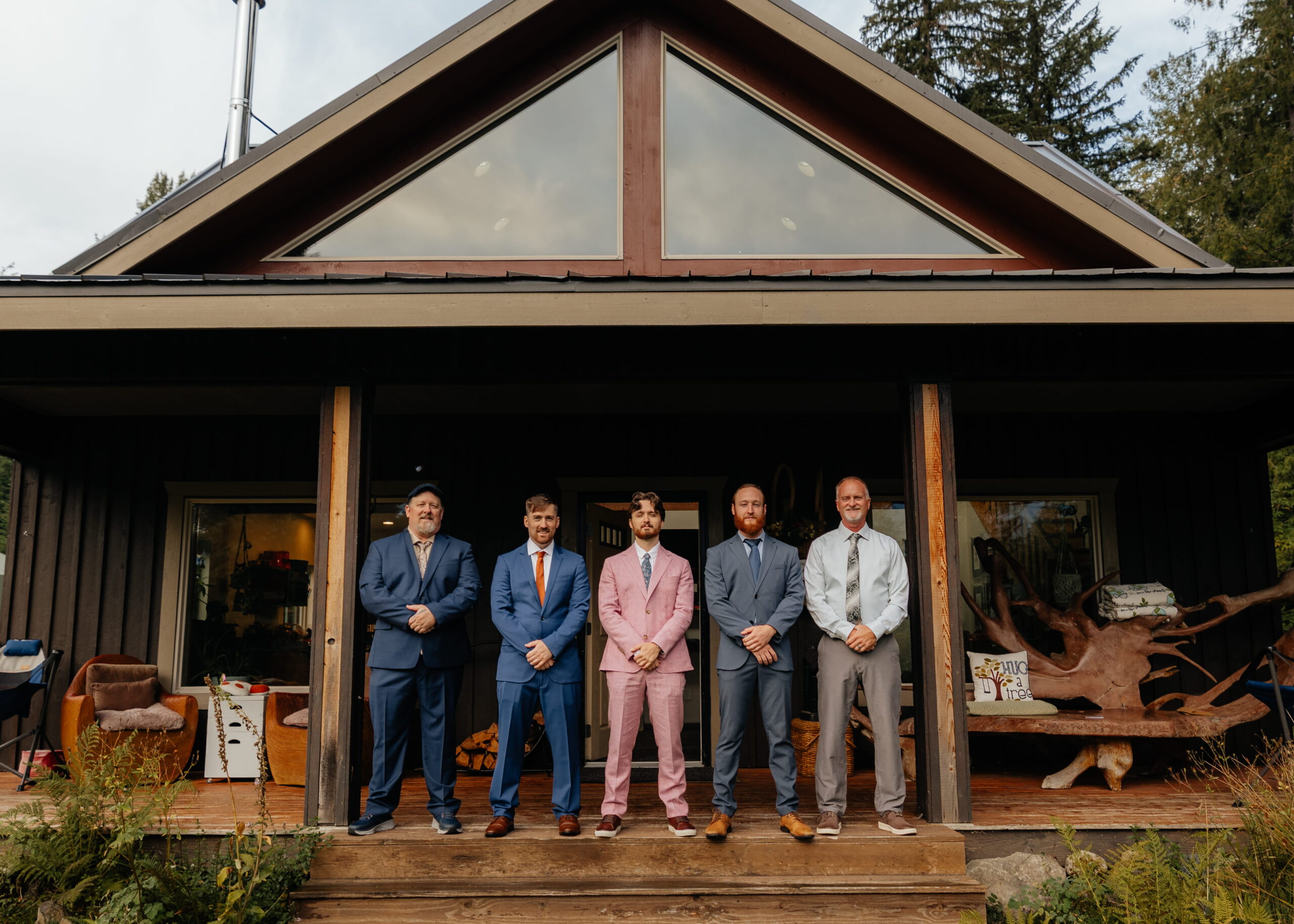 Groom stands on the front porch of a cabin with his friends and family.