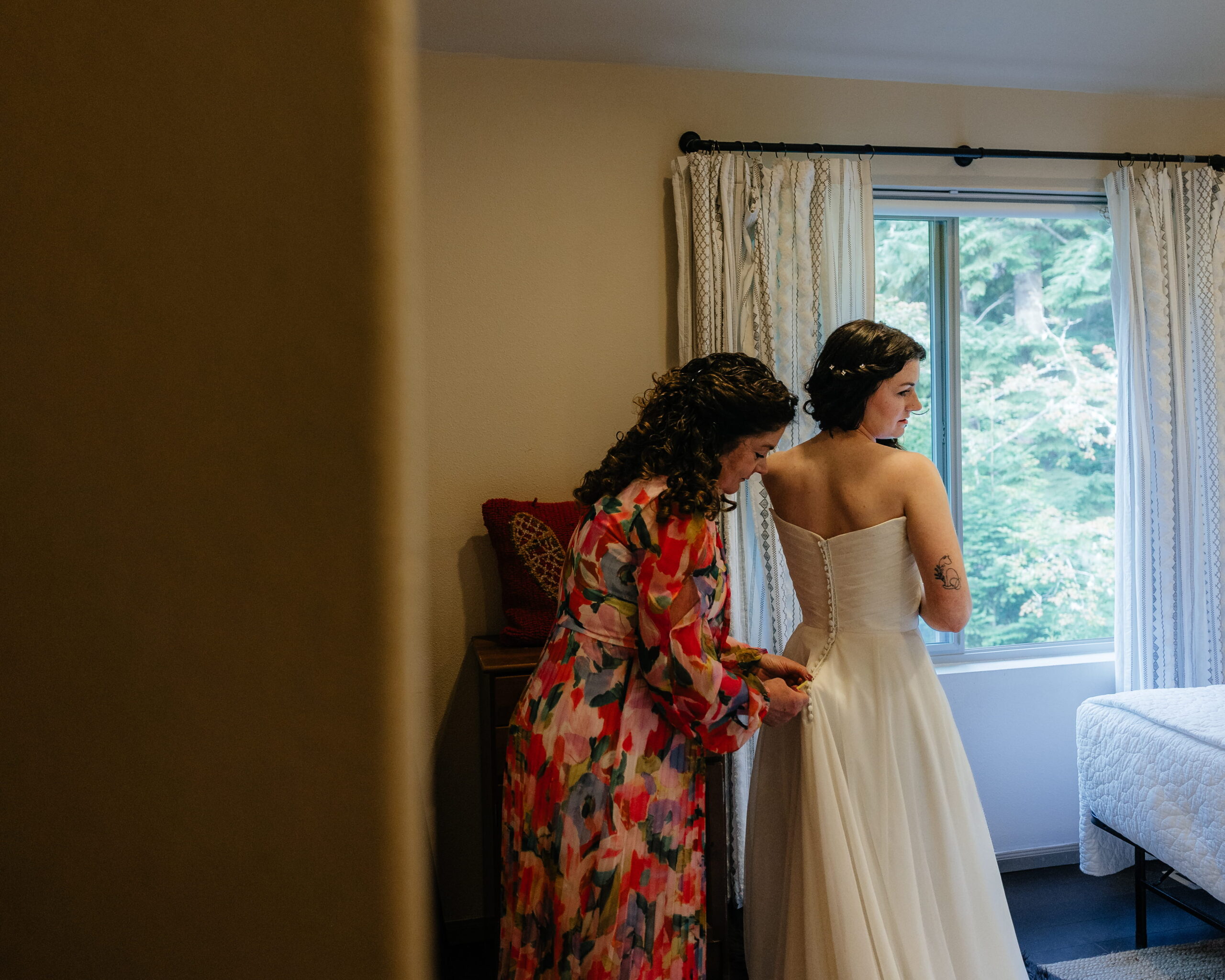 Woman helps bride zip up her wedding dress.