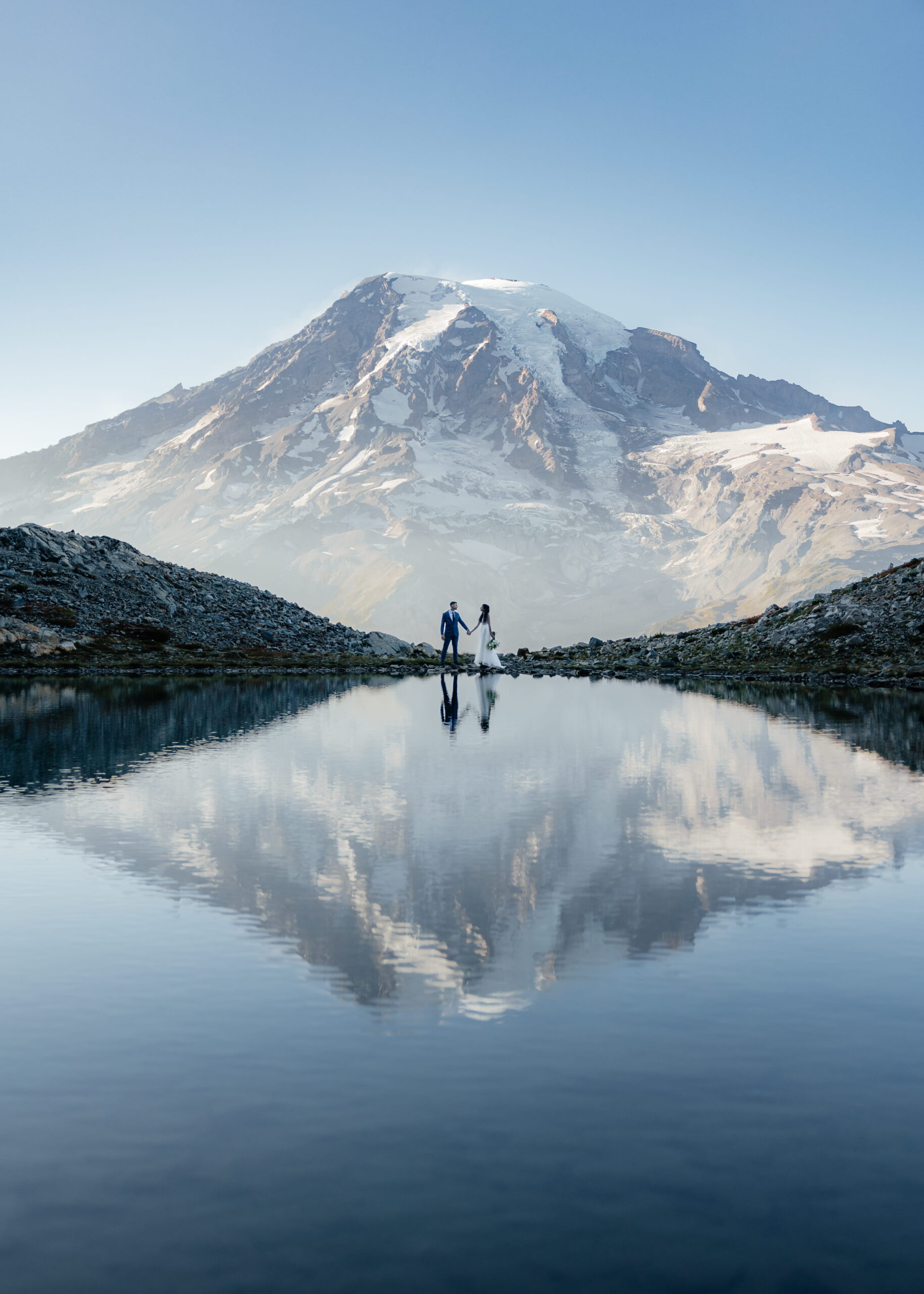 Newlyweds hold hands in front of a reflection lake at Mt Rainier National Park during their elopement.