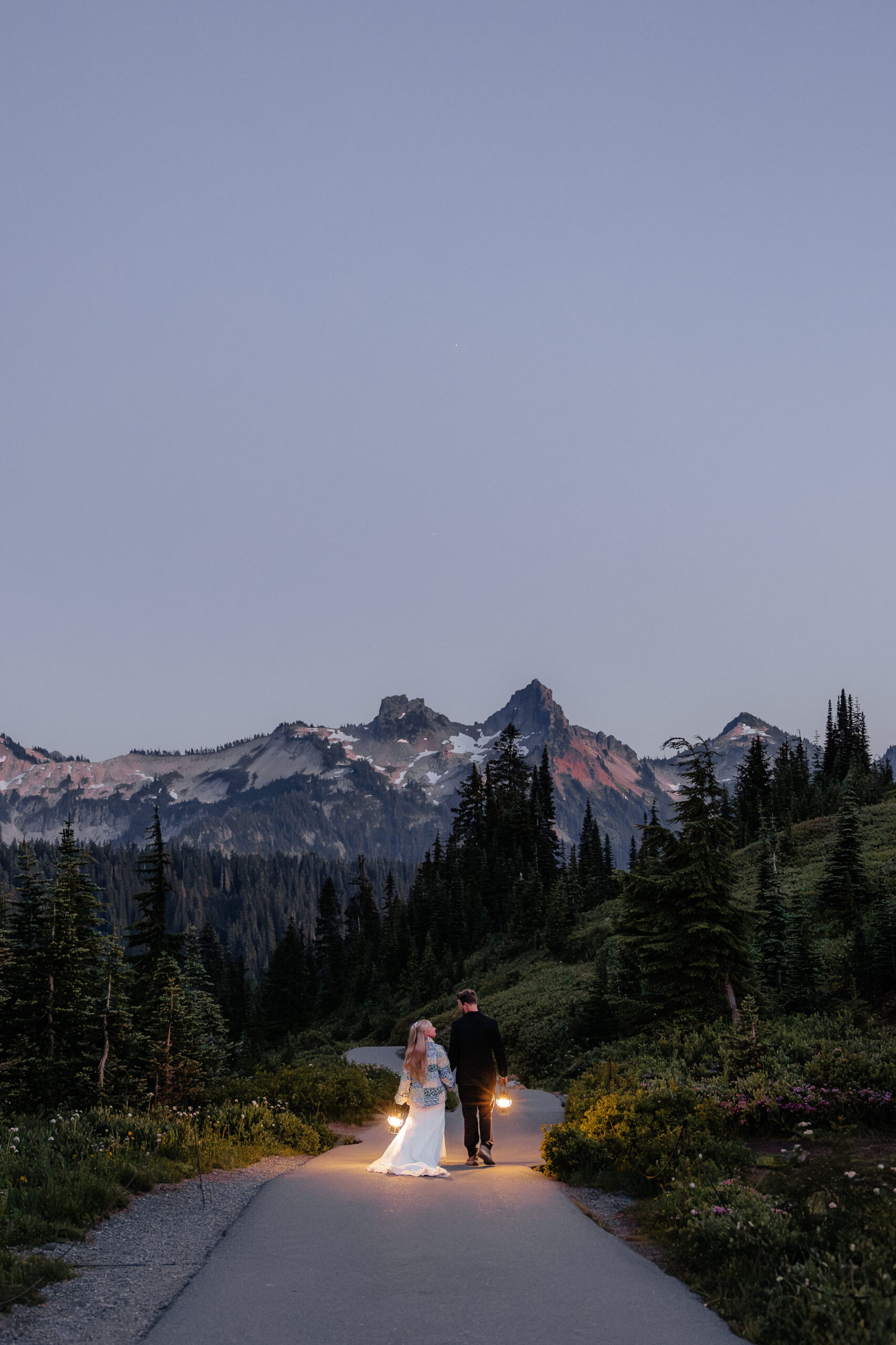 Couple holds lanterns while walking down a pathway in Mt Rainier National Park.